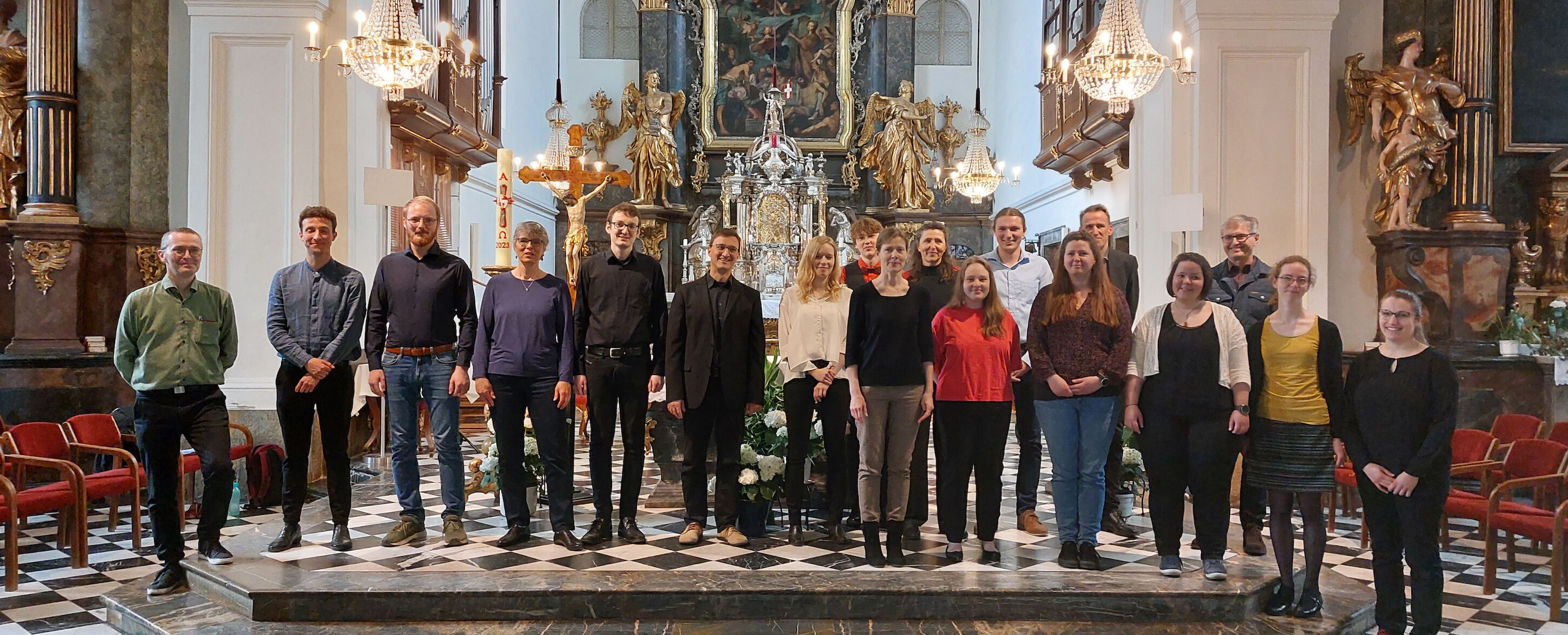 Eine Gruppe von Menschen steht in einer Kirche mit kunstvollen Verzierungen und Kronleuchtern.