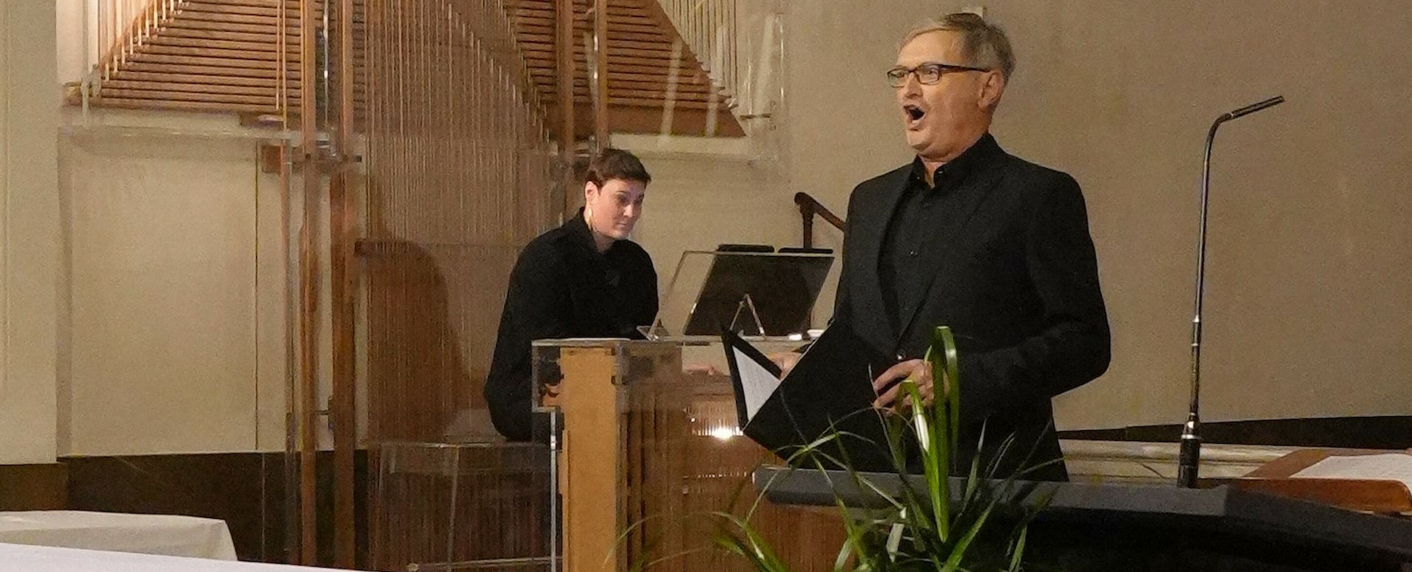 Ein Mann singt, während eine andere Person in einer Kirche Orgel spielt.