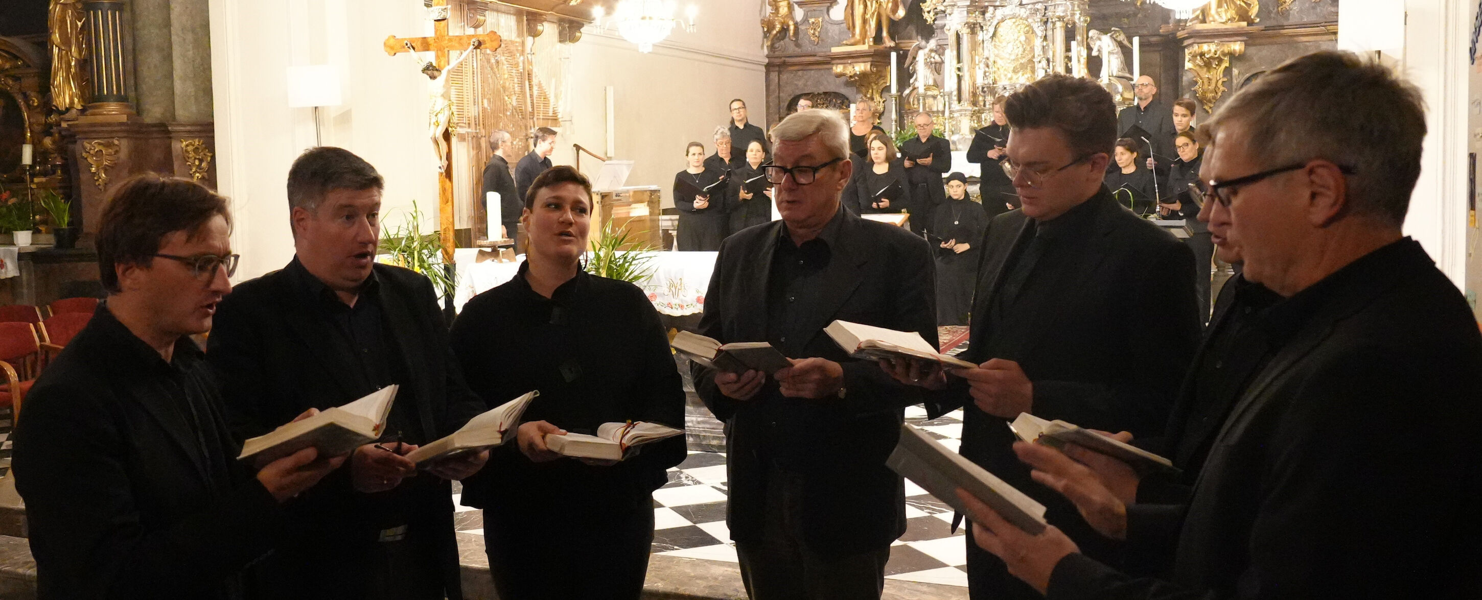 Eine Gruppe von Menschen singt in einer Kirche aus Büchern, während andere im Hintergrund auftreten.