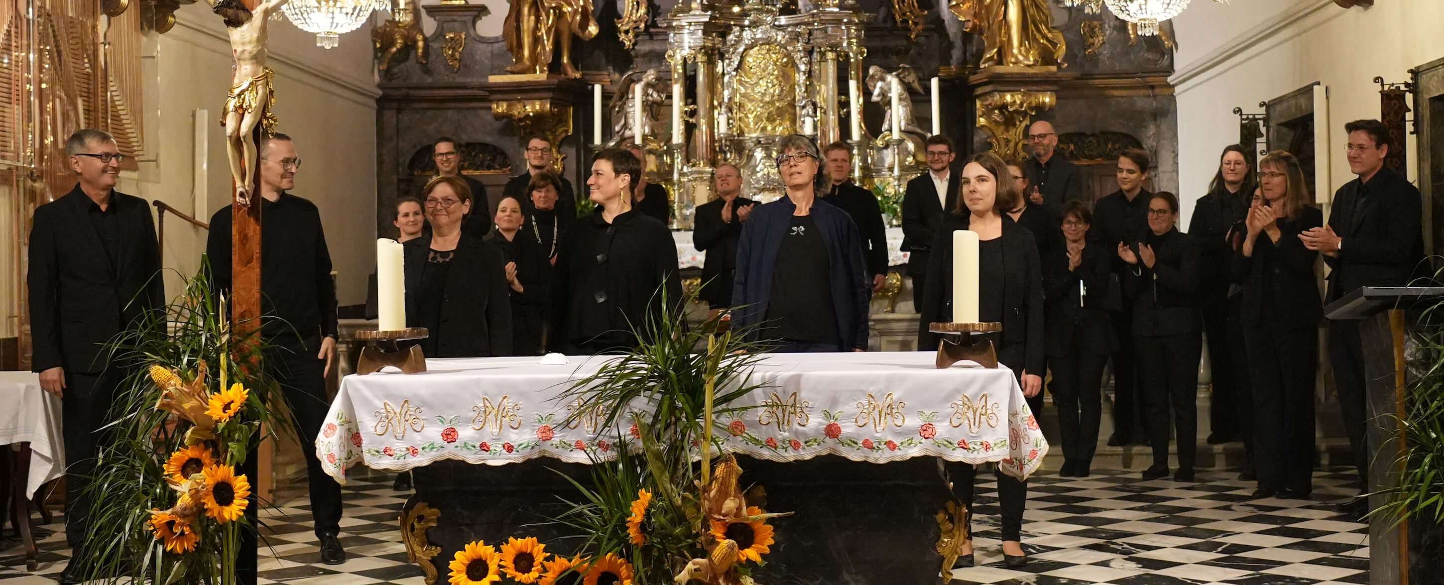 Chormitglieder stehen und applaudieren in einer geschmückten Kirche vor einem Altar mit Blumen.