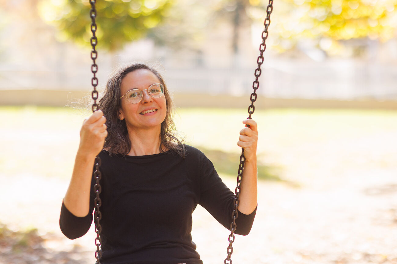 Frau mit Brille sitzt auf einer Schaukel im Freien in einem sonnigen Park.