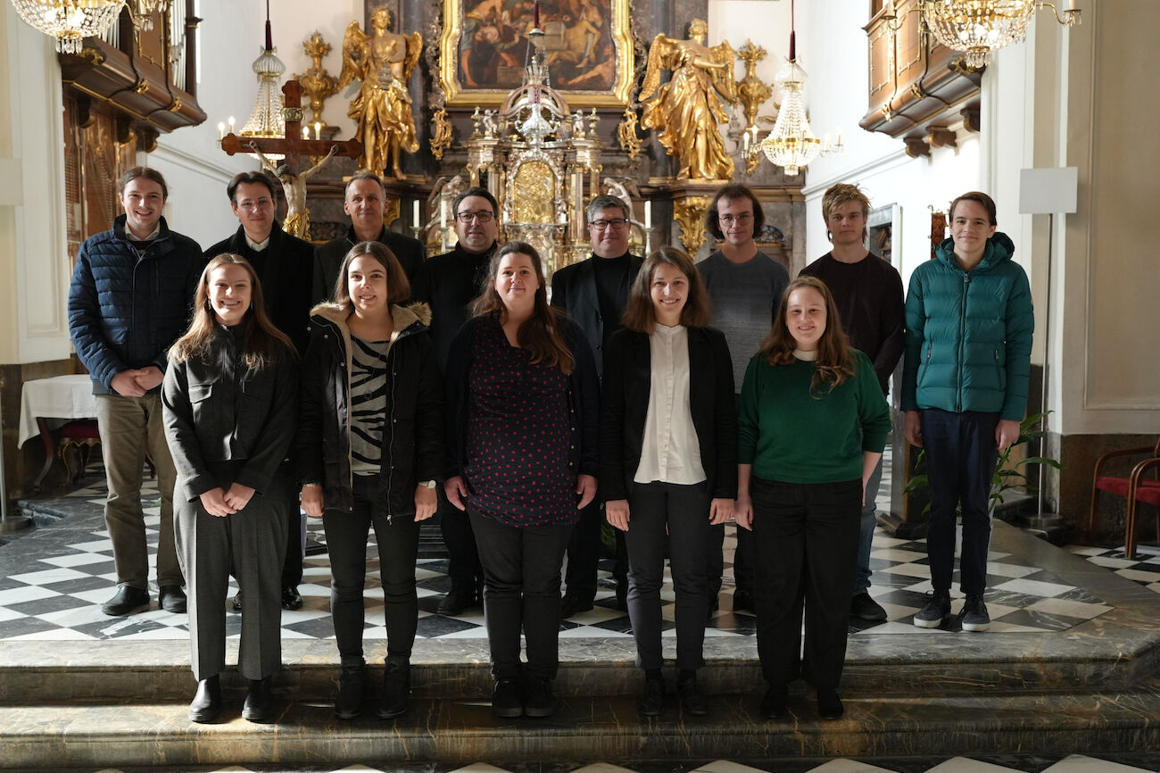 Eine Gruppe von dreizehn Personen posiert für ein Foto in einer reich verzierten Kirche mit Goldverzierungen.