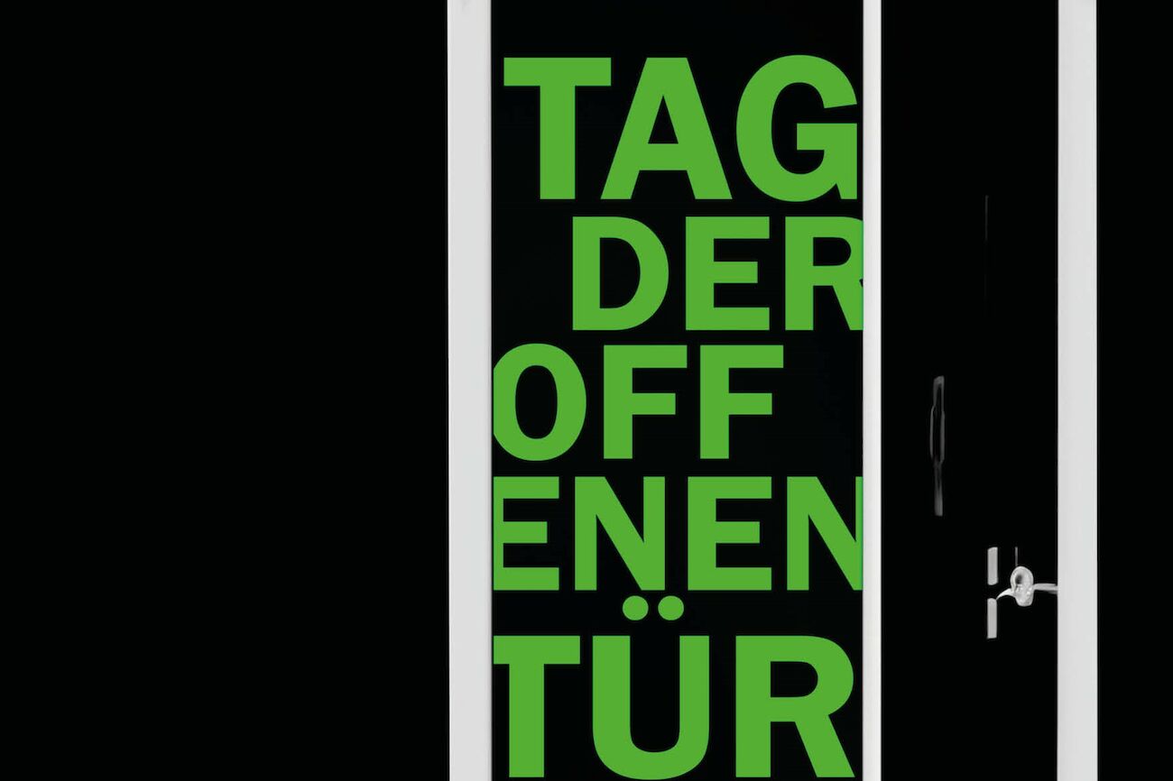 Grüner deutscher Text „Tag der offenen Tür“ auf einer schwarzen Tür mit weißem Rahmen und Griff.