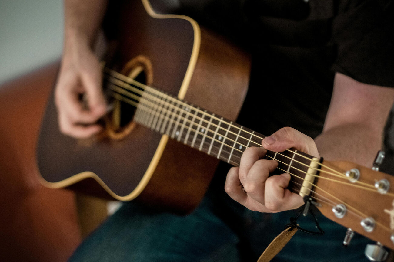 Person, die eine Akustikgitarre spielt und sich auf ihre Hände und die Gitarrensaiten konzentriert.